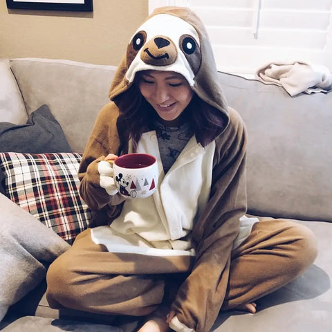 Mädchen trägt einen Faultier-Kigurumi, während sie zu Hause Kräutertee genießt